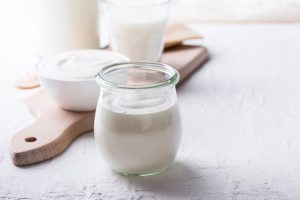 UV decontamination for dairy products, packaging and facilities Unlabeled glass of yogurt in the foreground with a ceramic bowl of yogurt and a glass of milk in the background, highlighting UV decontamination of dairy products, packaging, surfaces, air and water.