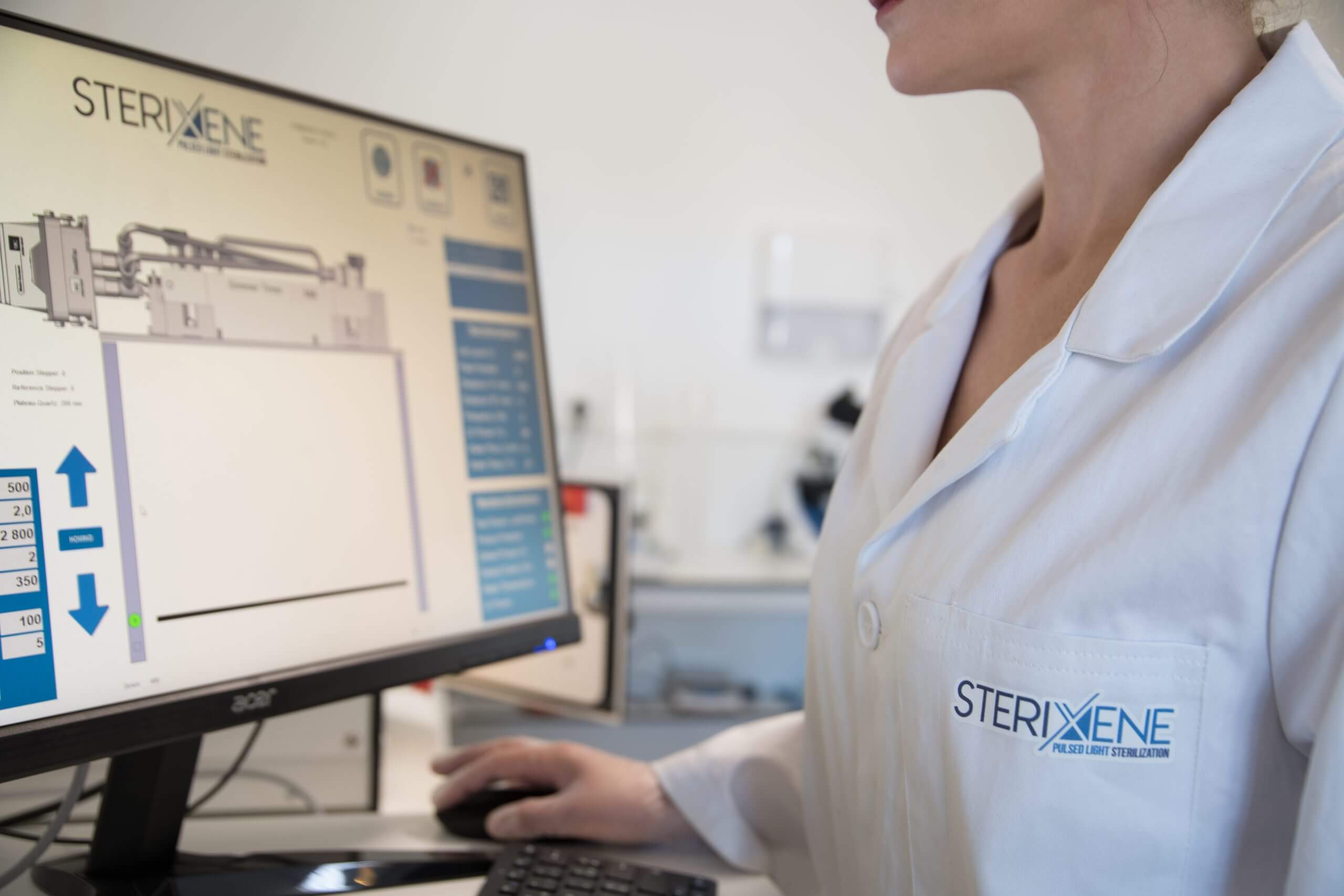 Laboratory workstation with a computer displaying a UV pulsed light system, microbiology testing data on screen and a lab technician using the mouse.